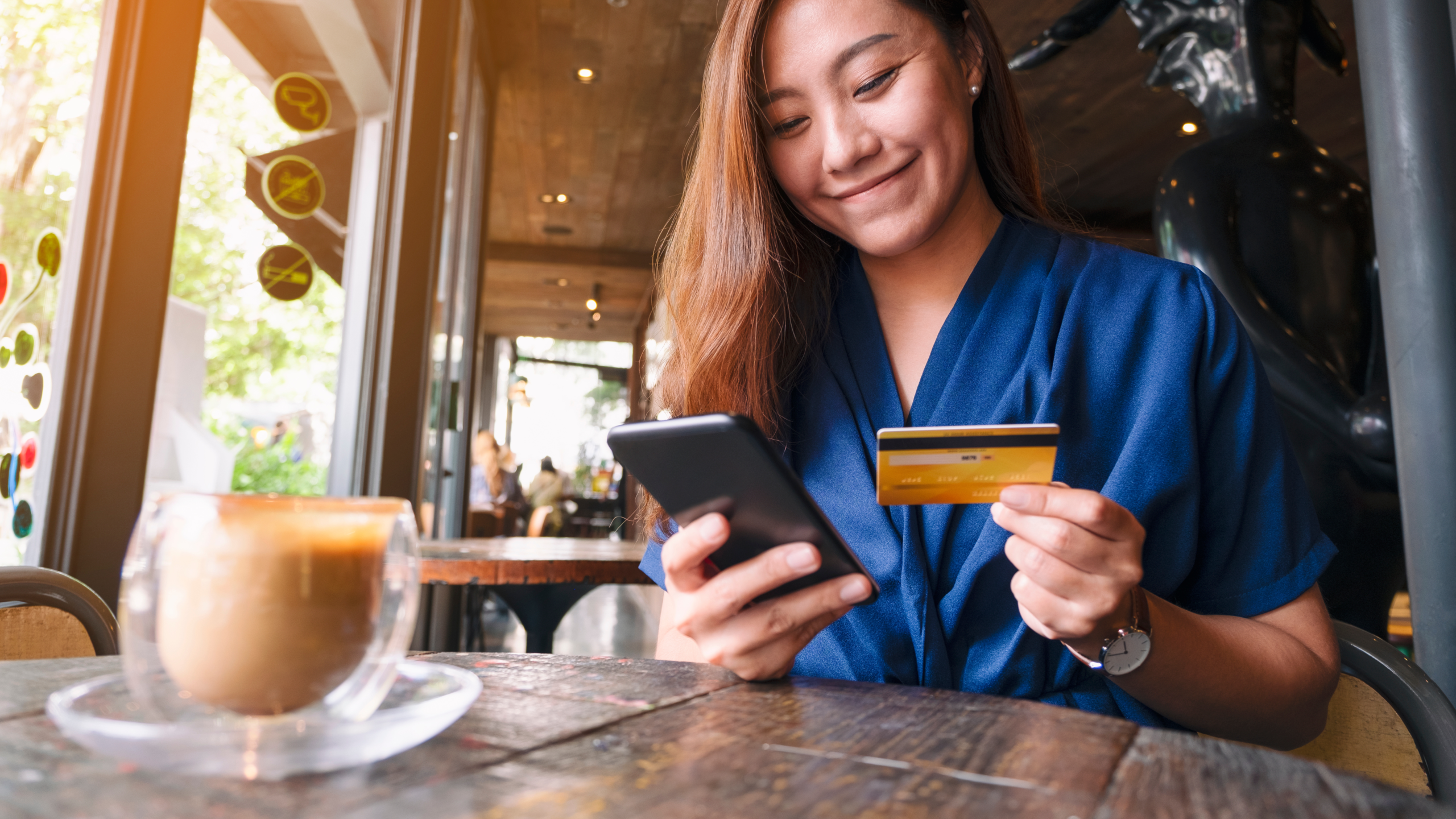 Woman holds a credit card and a phone in a resturant.
