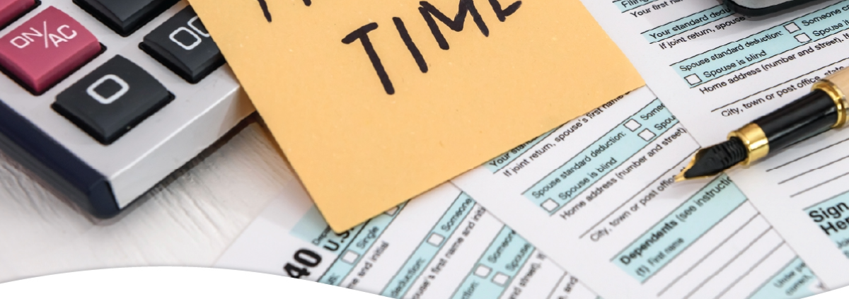 Calculator and tax forms with a sticky note on top with the words Tax Time.