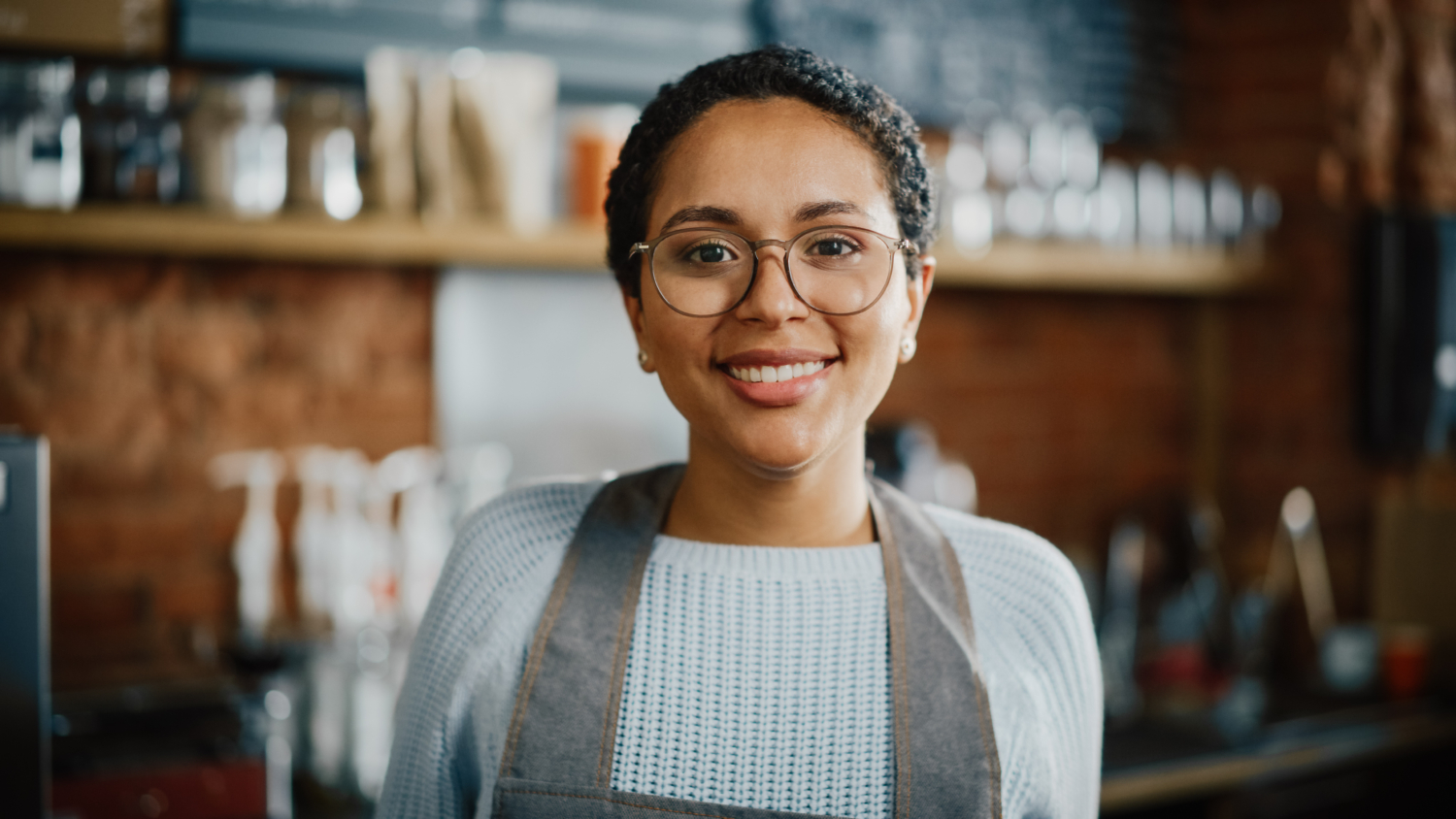 Business-Checking-Control-Low-Cost-Easy-Access-Owner Smiling female small business owner/barista, illustrating the control, low cost, and easy access of our business checking.