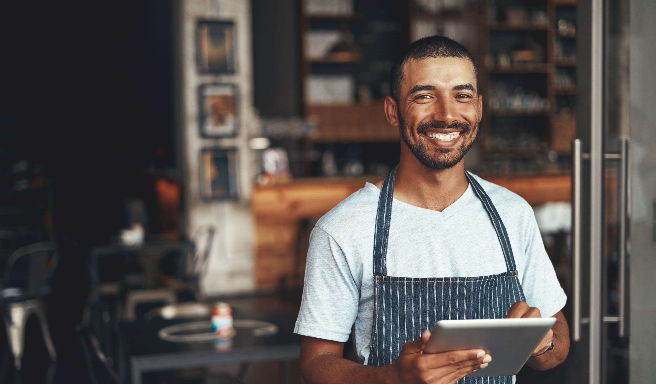 Smiling small business owner holding a tablet, representing financial control and savings accounts for business goals.