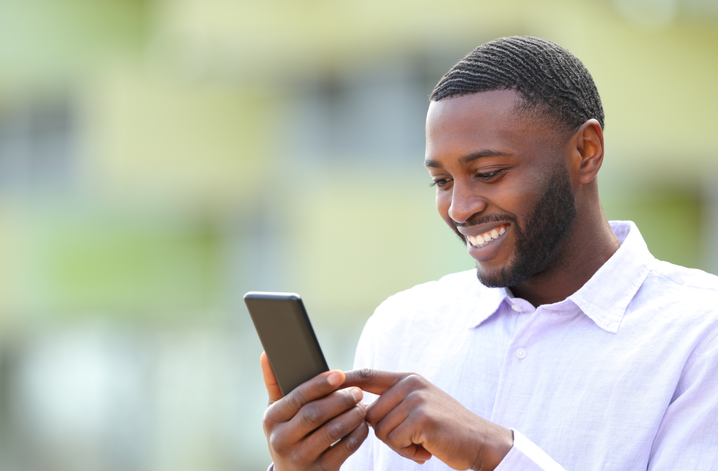 Smiling man using a smartphone outdoors to access a mobile banking app and manage his money.