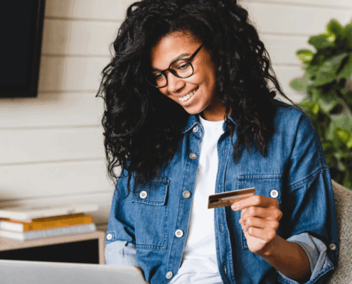 Cheerful african young woman doing online shopping at home using laptop and credit card. African-american woman paying bills online